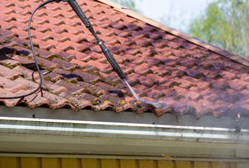 Man is washing the moss from the roof with a high pressure washer. House maintenance work.