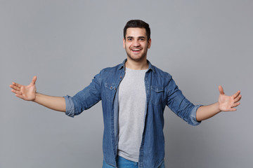Handsome stylish unshaven young man in denim jeans shirt posing isolated on grey wall background...