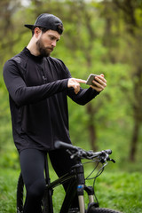 Young sportsman riding bicycle, holding smartphone, sunny park