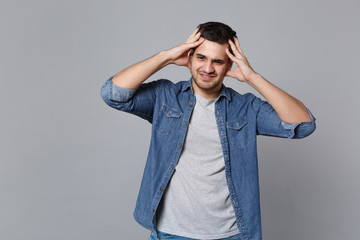 Angry mad sad upset unshaven young man in denim jeans shirt posing isolated on grey wall background studio portrait. People sincere emotions lifestyle concept. Mock up copy space. Screaming gesturing.