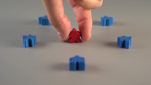 A hand removes a red shape from the surroundings of blue shapes on a gray surface. Concept of firing a leader from a team