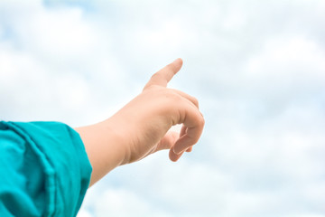 Child hand with exposed index finger raised up over blue sky and clouds. Gesture