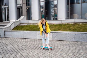 Blond female hipster woman riding on the longboard in the street at city.
