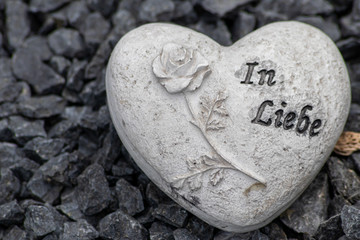 Weißes Steinherz mit Rose und Inschrift In Liebe auf einem Grab auf einem Friedhof als Andenken an...