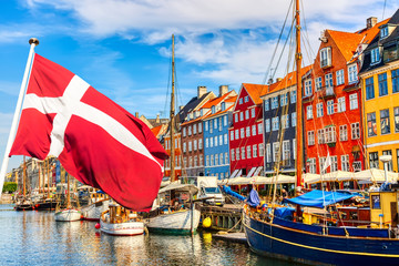 Copenhagen iconic view. Famous old Nyhavn port in the center of Copenhagen, Denmark during summer sunny day with Denmark flag on the foreground. - obrazy, fototapety, plakaty