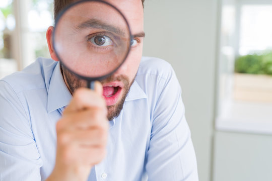 Handsome business man holding magnifying glass close to face, big eyes and funny expression
