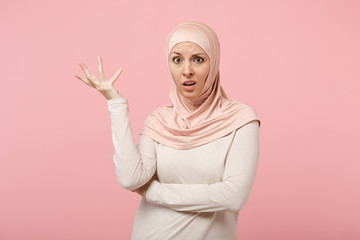 Perplexed bewildered young arabian muslim woman in hijab light clothes posing isolated on pink background studio portrait. People religious Islam lifestyle concept. Mock up copy space. Spreading hand.