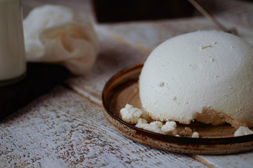 Homemade cottage cheese lies on a ceramic plate close-up on a wooden textured background.
