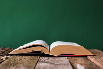 Back to school concept, open book on old wooden surface against a backdrop of clean green chalk board, selective focus, copy space