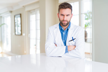 Handsome doctor man wearing medical coat at the clinic skeptic and nervous, disapproving expression on face with crossed arms. Negative person.