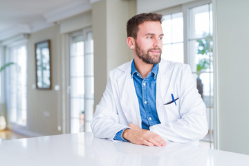 Fototapeta premium Handsome doctor man wearing medical coat at the clinic looking away to side with smile on face, natural expression. Laughing confident.