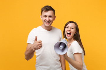 Cheerful young couple friends guy girl in white blank empty t-shirts posing isolated on yellow...