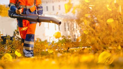 Male worker removes leaf blower leaves lawn of garden Autumn