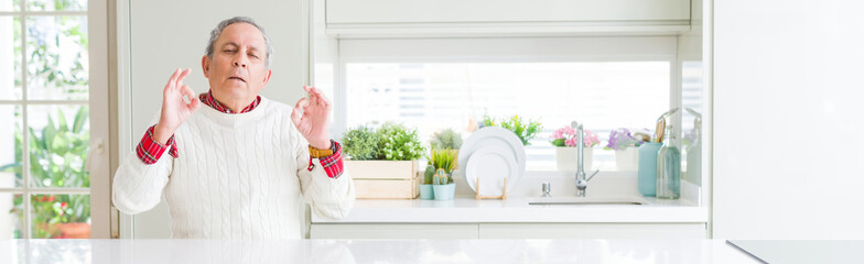 Wide angle perspective of handsome senior man at home relax and smiling with eyes closed doing meditation gesture with fingers. Yoga concept.