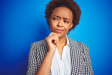 African american business executive woman over isolated blue background with hand on chin thinking...