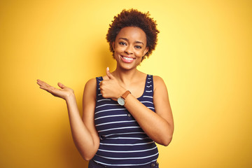 Beauitul african american woman wearing summer t-shirt over isolated yellow background Showing palm hand and doing ok gesture with thumbs up, smiling happy and cheerful