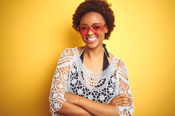 Young african american woman with afro hair wearing bikini and heart shaped sunglasses happy face smiling with crossed arms looking at the camera. Positive person.