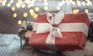 Big red present over Christmas lights bokeh in home on wooden table. Holiday decoration, magic Christmas