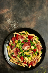 Penne pasta with grilled vegetables and prosciutto. Top view with copy space.