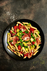 Penne pasta with grilled vegetables and prosciutto. Top view with copy space.