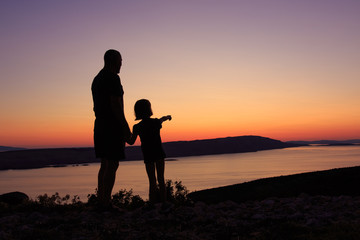 Fototapeta na wymiar Silhouette of a grandfather and his granddaughter enjoying the sunset view at the sea on a Croatian coast