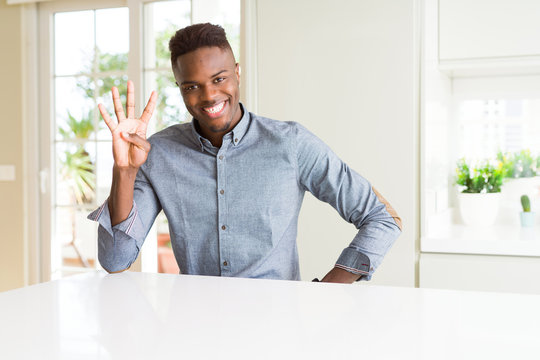 Handsome african american man on white table showing and pointing up with fingers number four while smiling confident and happy.