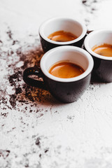 Three cups of freshly brewed espresso coffee on a textured table top with copyspace