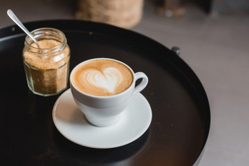 One cup of cappuccino with latte art on black table, white ceramic cup, top view. Cafe culture.