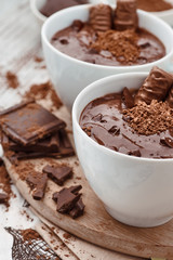 Two mugs of a hot chocolate with chocolate sticks on a wooden board