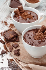 Two mugs of a hot chocolate with chocolate sticks on a wooden board