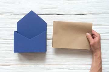 Man hand is holding a blank letter page near a post box on a white wooden background.
