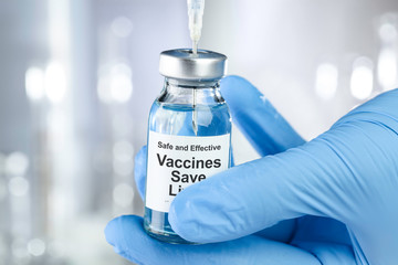 Healthcare concept with a hand in blue medical gloves holding a vaccine vial wtih the words Safe and Effective, Vaccines Save Lives, and does not cause autism