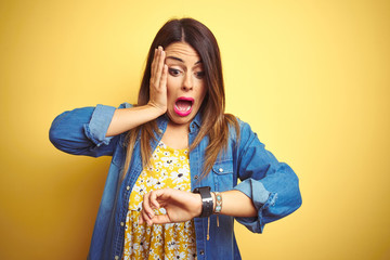 Young beautiful woman standing over yellow isolated background Looking at the watch time worried, afraid of getting late - obrazy, fototapety, plakaty