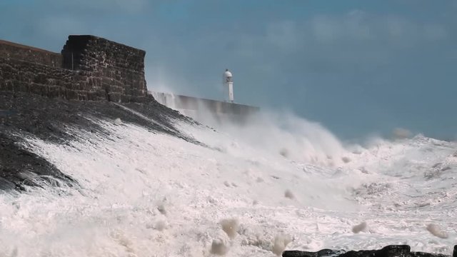Huge ocean waves and surf crashing against a sea wall and lighthouse (Porthcawl, South Wales)