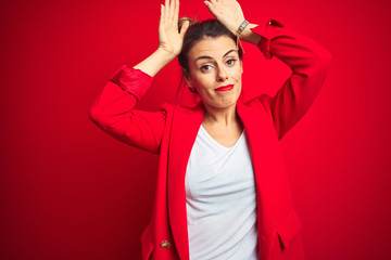 Young beautiful business woman standing over red isolated background Doing bunny ears gesture with hands palms looking cynical and skeptical. Easter rabbit concept.