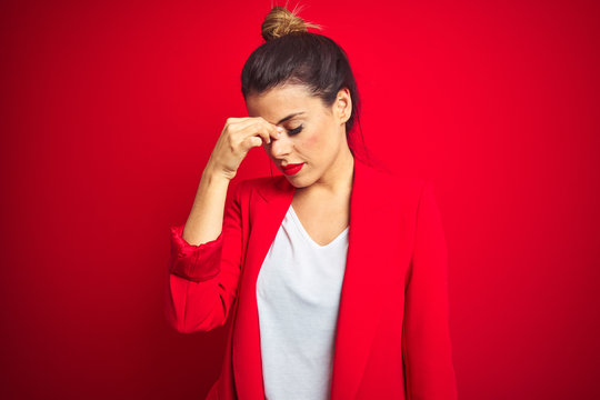 Young beautiful business woman standing over red isolated background tired rubbing nose and eyes feeling fatigue and headache. Stress and frustration concept.