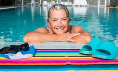 an old lady, amused, swimming to keep fit. outdoor pool with clear water and sunny day. Caucasian and smiling