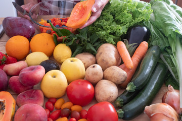 The hands of a senior woman choosing the best fruit for a fresh fruit salad. Wooden table with a large group of colorful fruits and vegetables. Healthy eating
