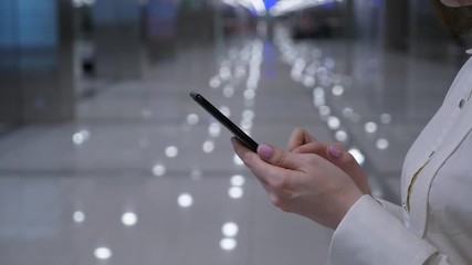 Business woman type message on mobile phone, blurred hall on background, close shot of smartphone in hands. Lady wear white shirt
