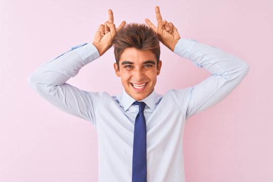 Young handsome businessman wearing shirt and tie standing over isolated pink background Posing funny and crazy with fingers on head as bunny ears, smiling cheerful