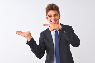 Young handsome businessman wearing suit standing over isolated white background amazed and smiling to the camera while presenting with hand and pointing with finger.