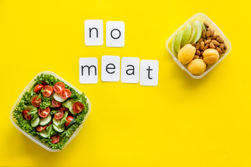 to-go box with salad, nuts, fruit and no meat text for vegetarian lunch on yellow background top view