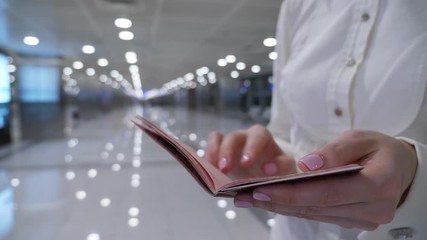 Woman thumb several empty pages of international passport and close it, blurred empty airport hall on background. Closeup shot of Russian ID in hands of female traveller