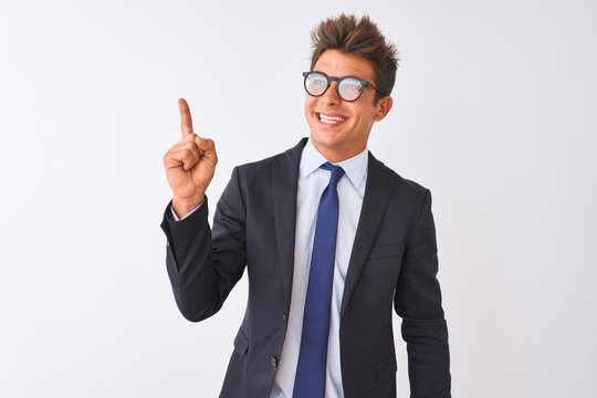 Young handsome businessman wearing suit and glasses over isolated white background with a big smile on face, pointing with hand and finger to the side looking at the camera.