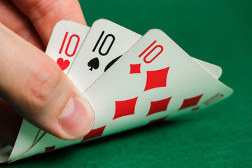 Hand holds a combination in poker - threee of a kind on a green background.