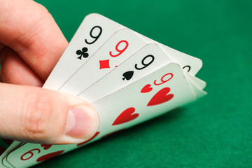 Hand holds a combination in poker - four of a kind on a green background.