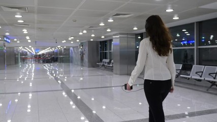 Passenger woman walk at empty airport passage, listen musing using large earphones, tracking shot, follow camera move beside behind lady. Modern international terminal sterile area, nobody seen around