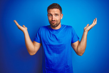 Young handsome man wearing casual t-shirt over blue isolated background clueless and confused...