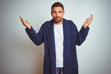 Young man wearing comfortable pajamas and robe at morning over isolated background clueless and...