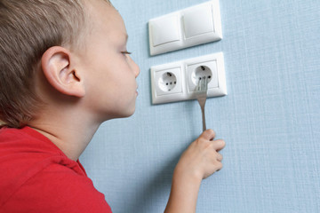 Child put fork in electric socket. Dangerous situation at home. Little boy playing with electrical...